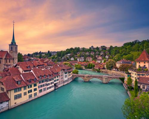 Panoramic sunset view of Bern's Old Town, with its historic red-roofed buildings lining the winding Aar River