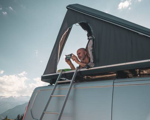 Man enjoying the view from a rooftop tent on a camper van in nature